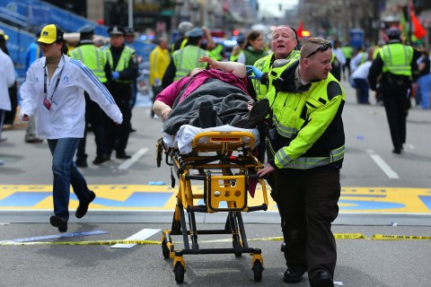 A woman who was injured in the first explosion is wheeled over the finish line of the Boston Marathon on Boylston Street, April 15, 2013.