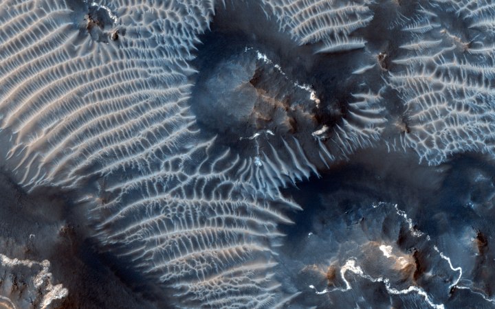 The Noctis Labyrinthus region of Mars, perched high on the Tharsis rise in the upper reaches of the Valles Marineris canyon system, on Sept. 26, 2013. Targeting the bright rimmed bedrock knobs, the image also captures the interaction of two distinct types of windblown sediments. Surrounding the bedrock knobs is a network of pale reddish ridges with a complex interlinked morphology. These pale ridges resemble the simpler transverse aeolian ridges (called TARs) that are common in the equatorial regions of Mars. Dark sand dunes comprise the second type of windblown sediment visible in this image.