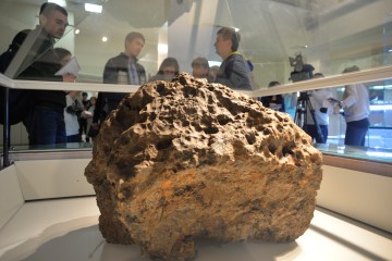 Reporters gather around a piece of a meteorite, which was lifted from the bottom of the Chebarkul Lake, placed on display in a local museum in Chelyabinsk, on Oct. 18, 2013.
